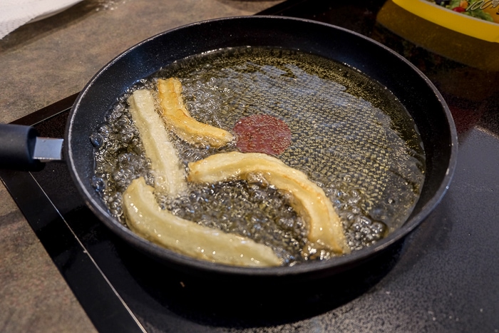 browning spanish churros dough in pan of bubbling oil