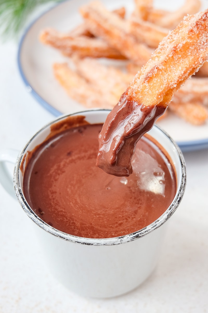 white mug of thick spanish hot chocolate with churros dipped in