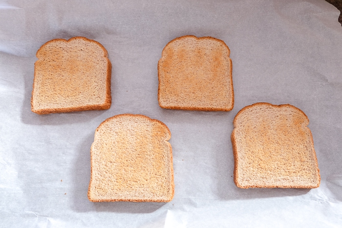four piece of bread on parchment paper on baking sheet