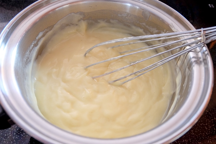 thickened vanilla pudding in silver pot with whisk on stove