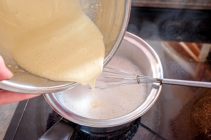 pouring vanilla pudding into milk in silver pot on stove