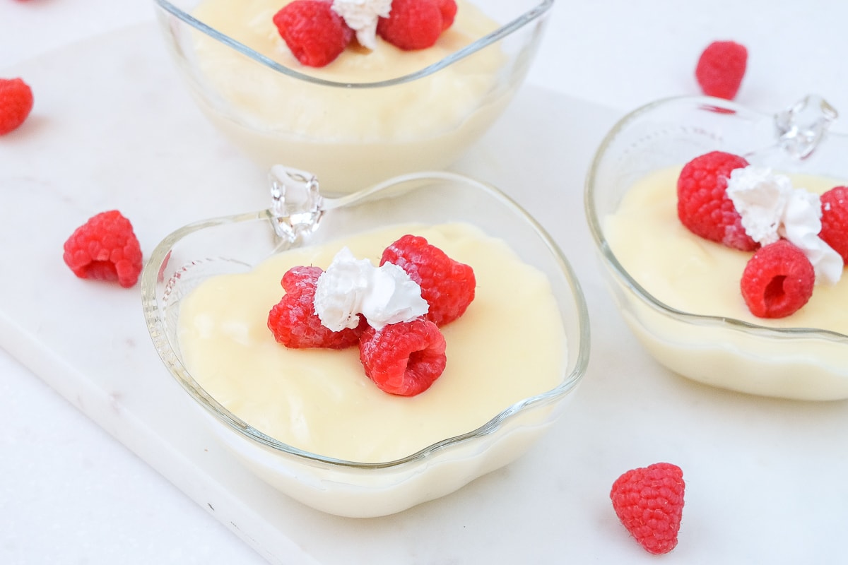 bowls of vanilla pudding with raspberries on top on white marble