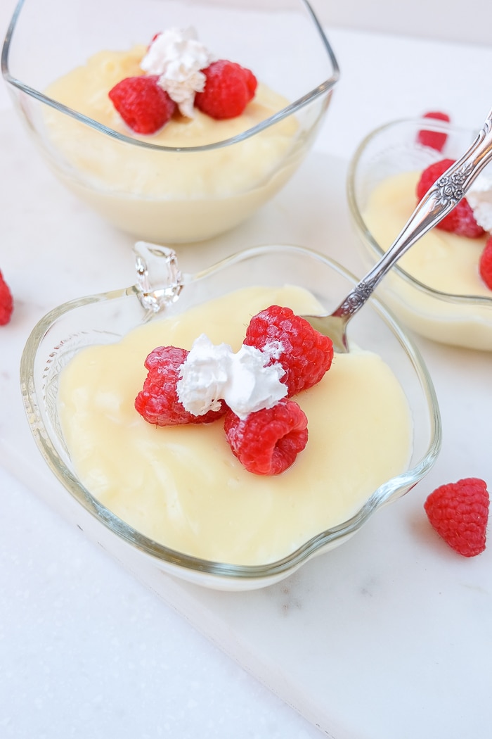 clear bowls of vanilla pudding with berries and a spoon in it