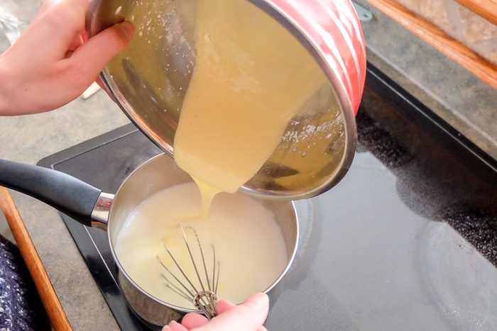 vanilla sauce mixture in bowl pouring into pot of milk with whisk
