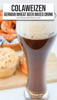 Dark beverage in wheat beer glass with cheese spread and pretzels in the background plus text overlay saying "Colaweizen German Wheat Beer Mixed Drink"