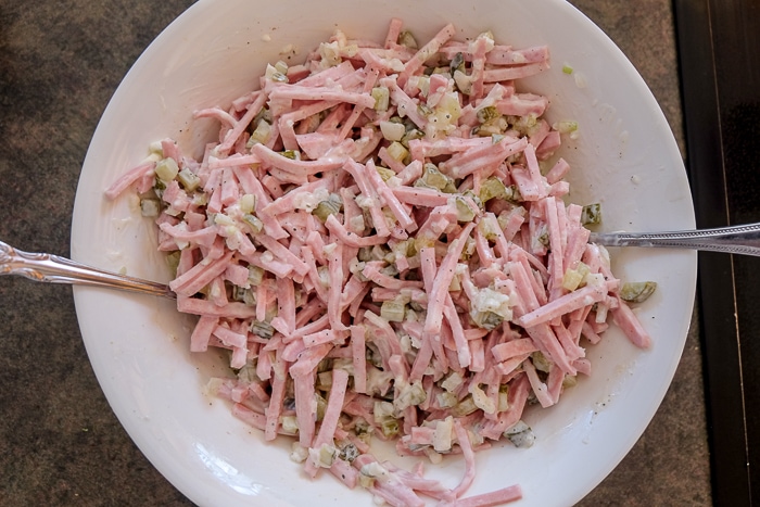 Fleischsalat mixed in white bowl with spoons on counter top