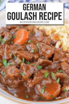 Beef chunks and carrot slices in brown sauce in bowl with parsley sprinkled on top and spaetzle noodles in the background plus text overlay saying "German goulash recipe"