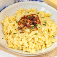 bowl of german kaesespaetzle with fried onions on wooden board