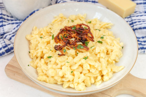 bowl of german kaesespaetzle with fried onions on wooden board