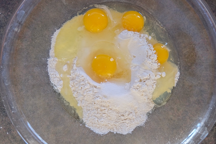 eggs cracked into clear bowl with flour ingredients
