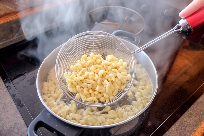 straining spoon lifting german spaetzle out of boiling pot on stove
