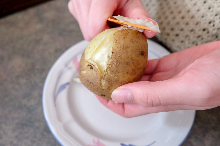 peeling boiled potato with knife in hand
