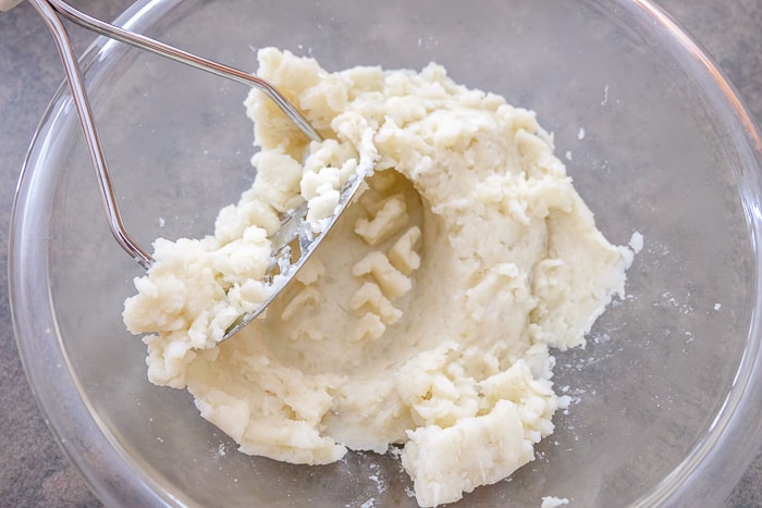 mashed potatoes in clear glass bowl with potato masher