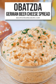 Photo of orange beer cheese spread in clear bowl with chopped parsley on top and text overlay saying "obatzda german beer cheese spread"