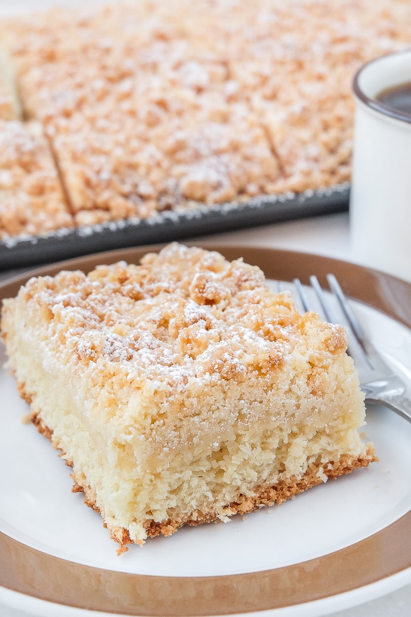 piece of crumb cake on plate with silver fork beside with sheet cake in background