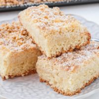 german crumb cake pieces stacked on plate with sheet cake behind
