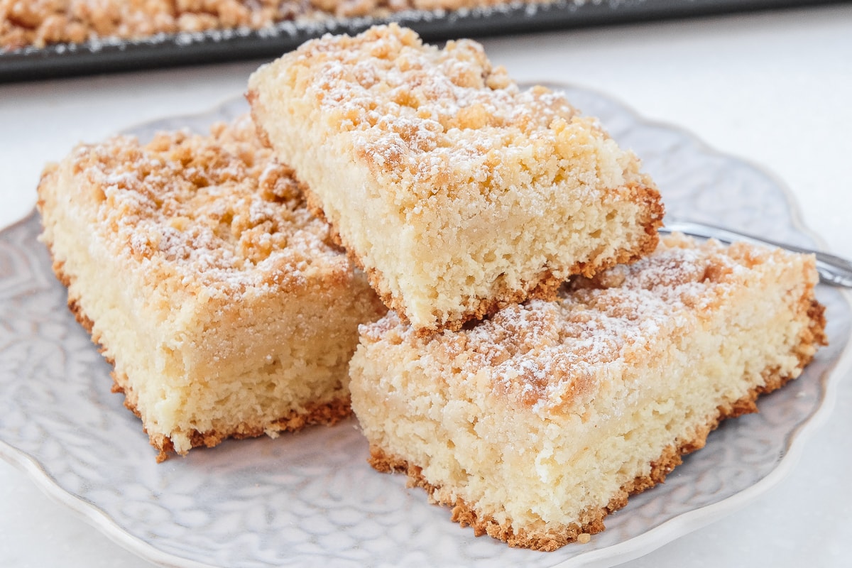 german crumb cake pieces stacked on plate with sheet cake behind