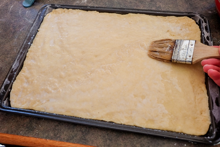 crumb cake dough brushed with milk on counter with paint brush beside