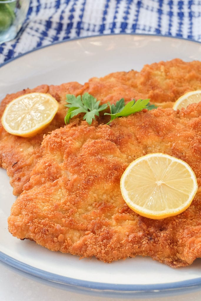 breaded german schnitzel on plate with slices of lemon on top