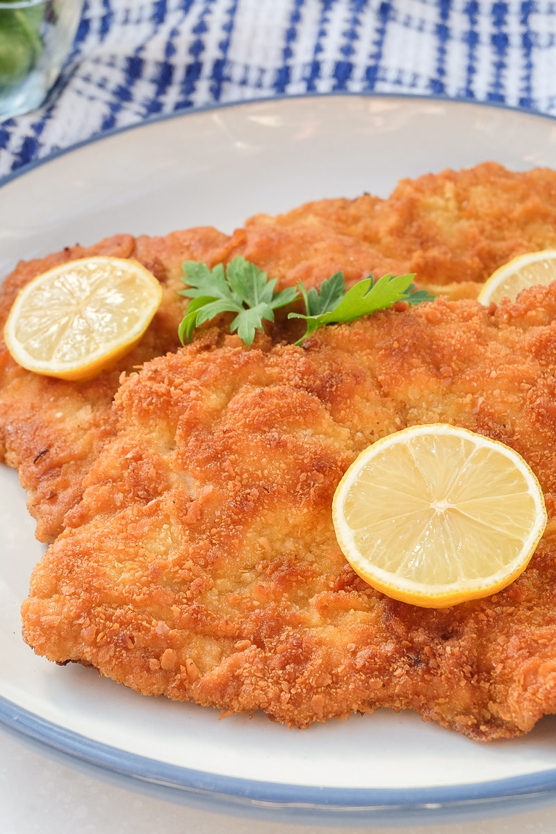 breaded german schnitzel on plate with slices of lemon on top