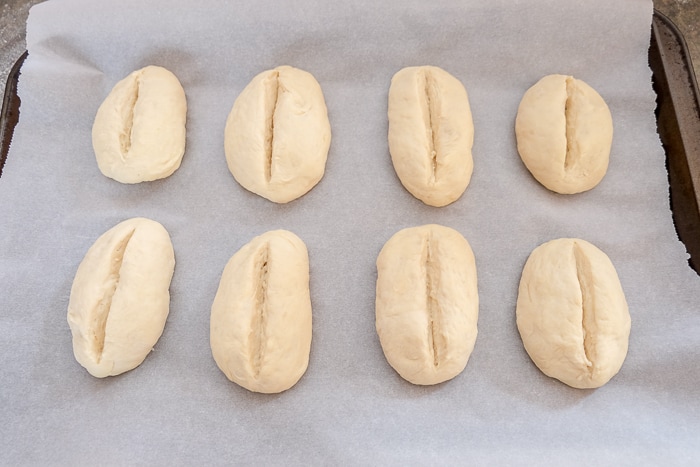 bread rolls with slits cut on top on parchment paper pan