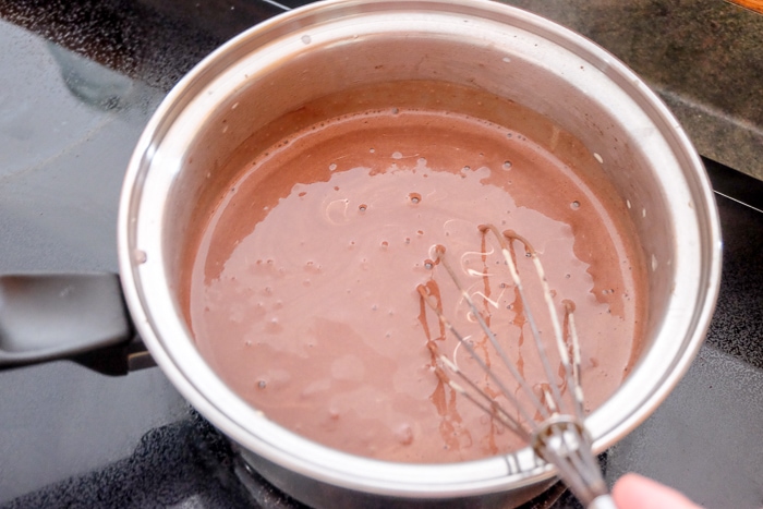 whisking thickening chocolate pudding in silver pot on stove