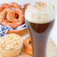 german colaweizen drink in tall glass with pretzels and cheese behind