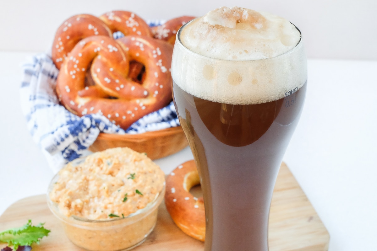 german colaweizen drink in tall glass with pretzels and cheese behind