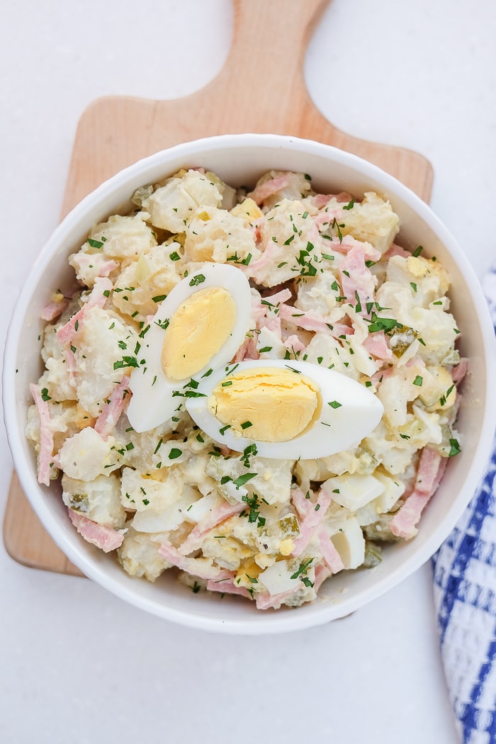 white bowl of german potato salad with sliced egg on top