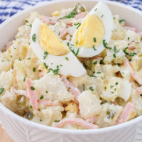 bowl of creamy german potato salad on wooden board with pickle behind