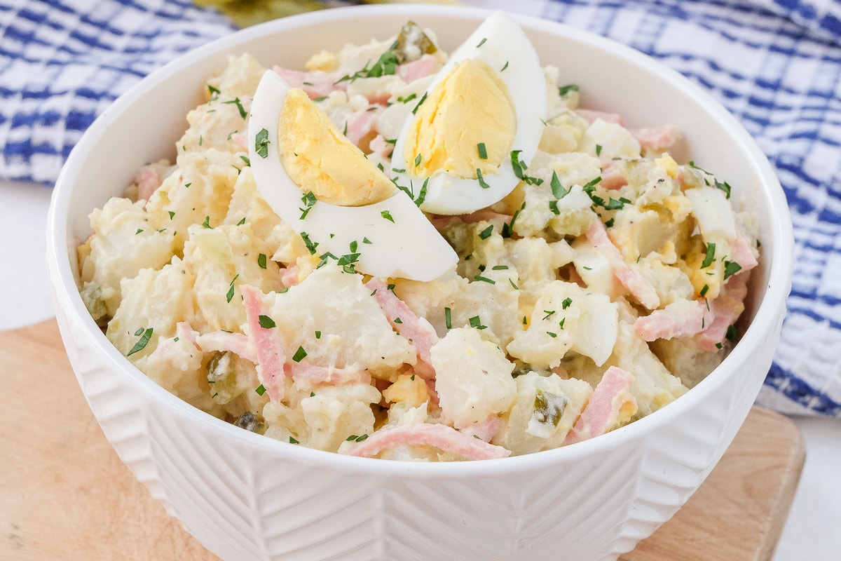 creamy potato salad in white bowl on wooden board with pieces of egg on top