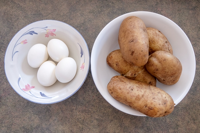 boiled potatoes and boiled eggs in white bowls on counter