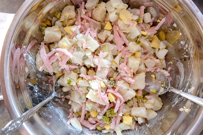 german creamy potato salad ingredients mixing in silver bowl with utensils