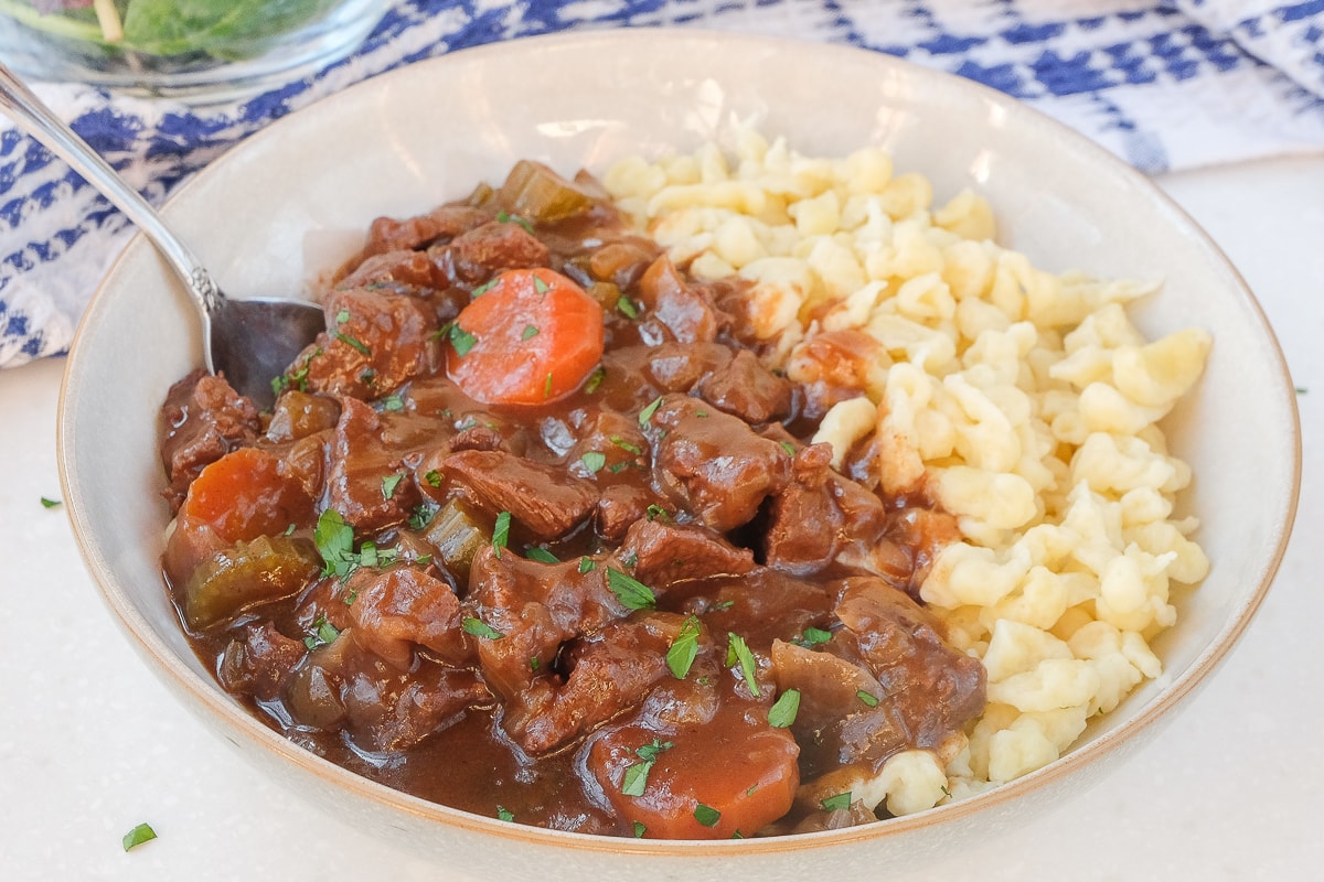 bowl of german beef goulash with spaetzle and fork beside on white counter top