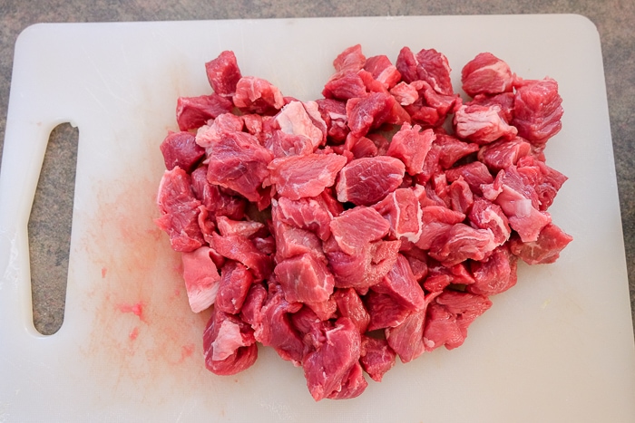 raw stewing beef cut into chunks on white plastic cutting board