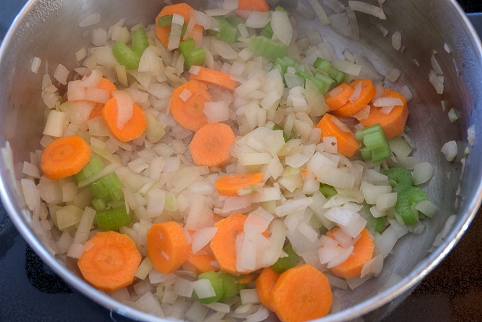 carrots and celery with onions cooking in silver pot on stove