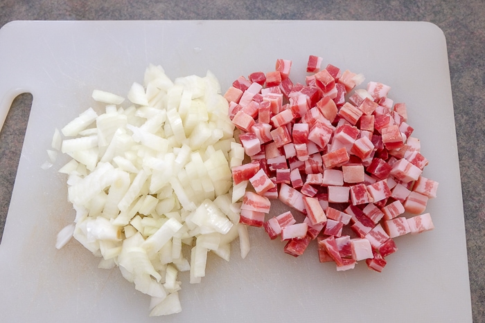 chopped onions and pancetta bacon on white plastic cutting board