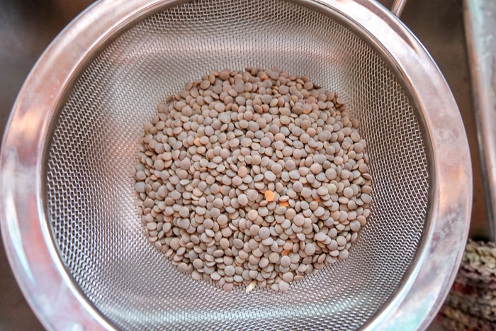 brown lentils in metal strainer over kitchen sink