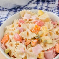 bowl of colorful pasta salad on wooden board with blue towel behind