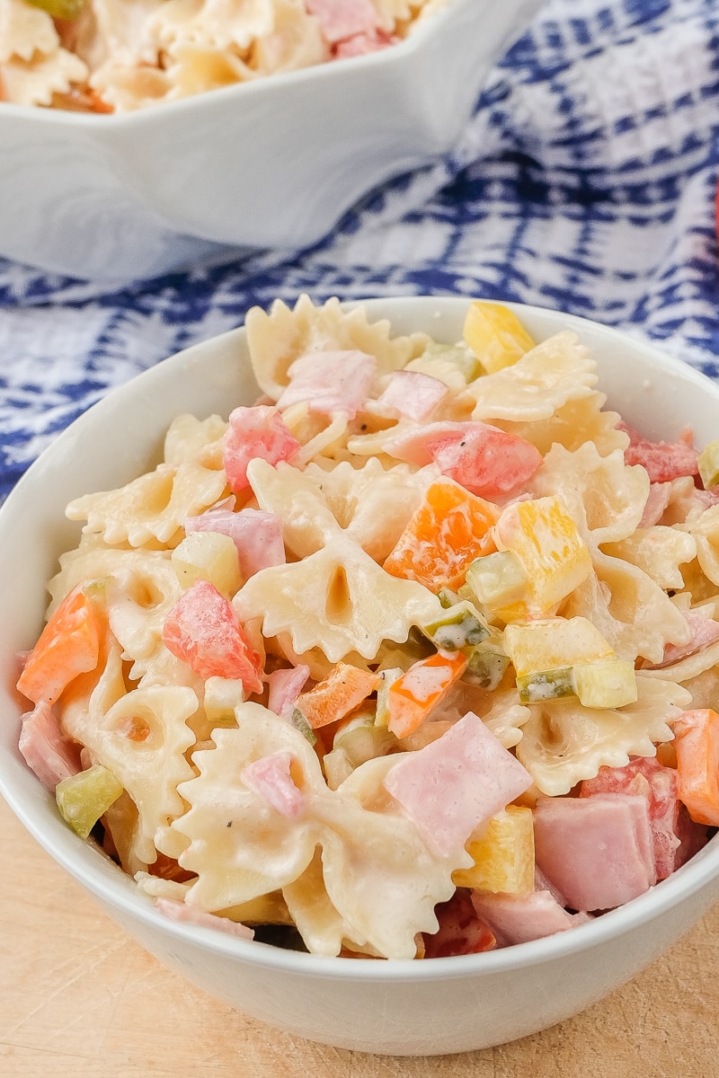 bowl of colorful pasta salad on wooden board with blue towel behind