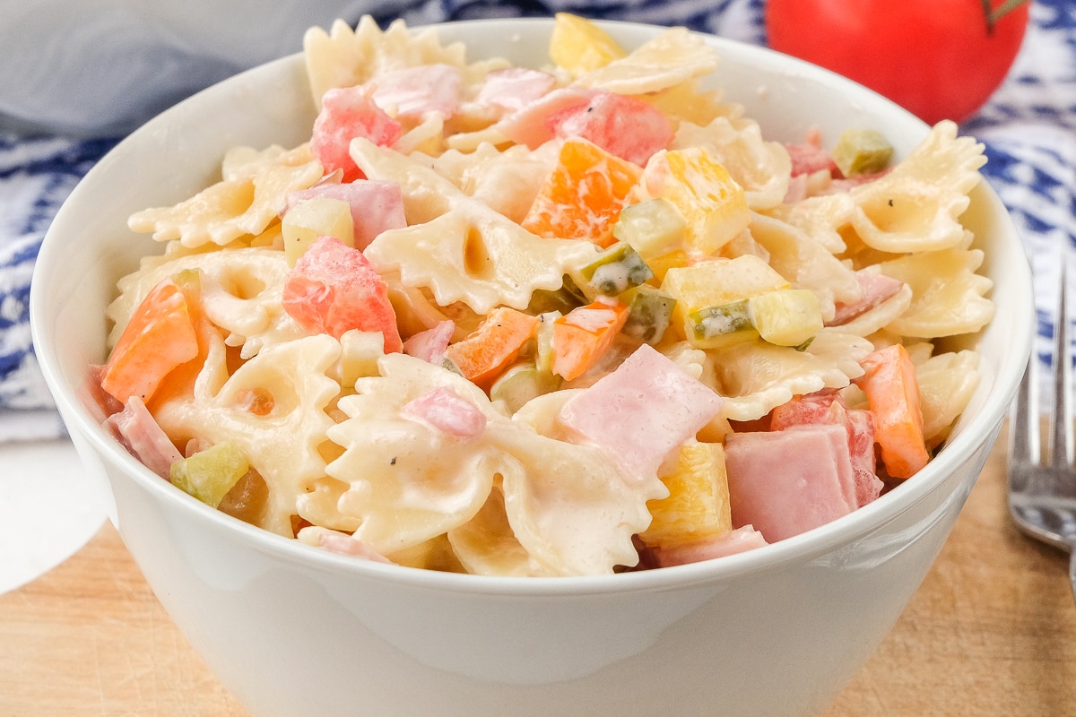 german pasta salad with bowties and peppers in white bowl on wood