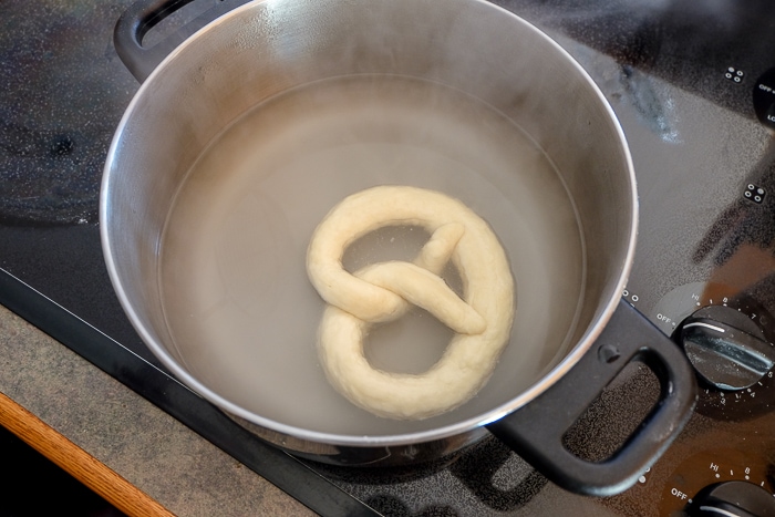 german pretzel floating in mixture in silver pot on stove top