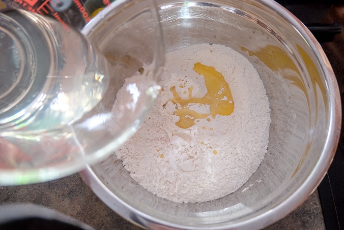measuring cup with water pouring into bowl of dry ingredients for german pretzels
