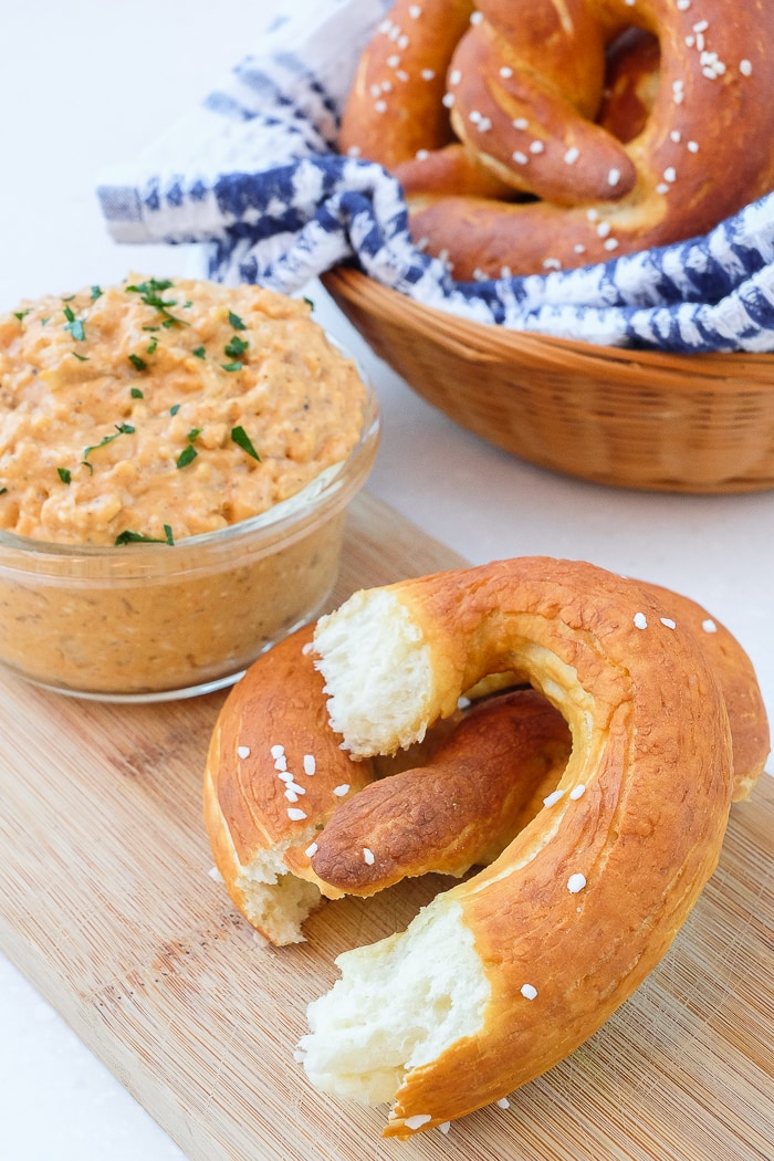 german pretzel on wooden board with obatzda spread and basket beside