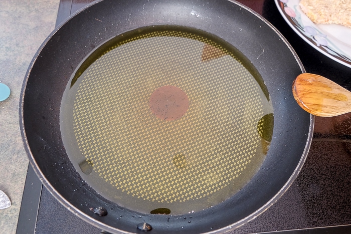 frying pan on stove with oil and wooden spoon beside