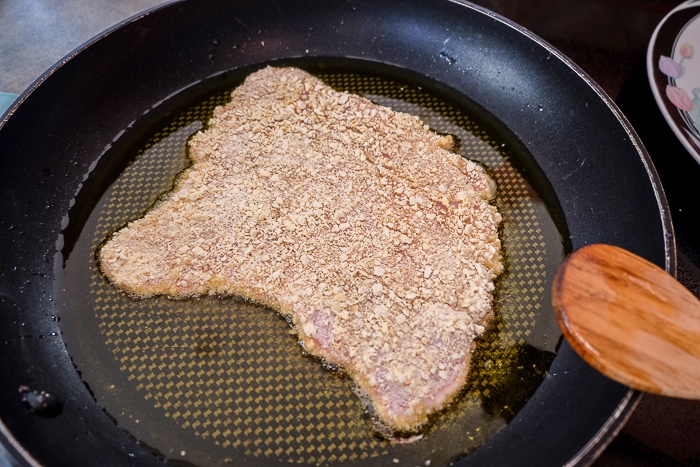 piece of pork schnitzel frying in lard in black frying pan