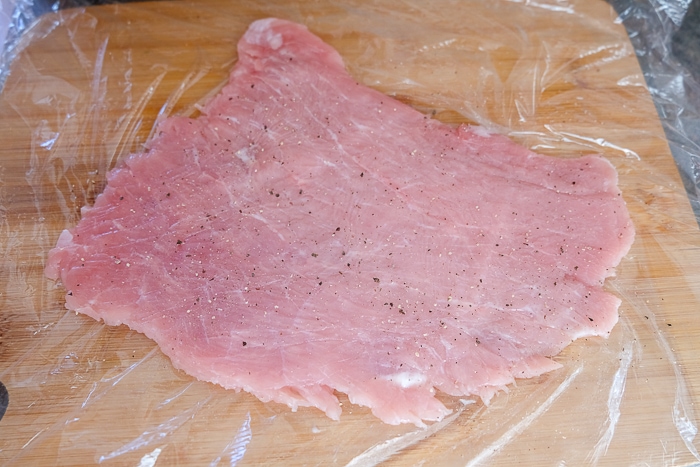 piece of raw pork schnitzel on wooden board with salt and pepper on it