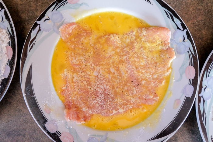 pork schnitzel in raw egg on plate