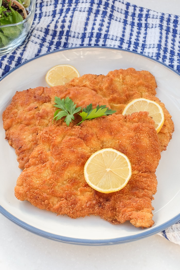 pieces of breaded german schnitzel with slices of lemon and parsley on top on plate