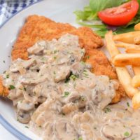 german jagerschnitzel on plate with mushroom sauce on top and fries beside